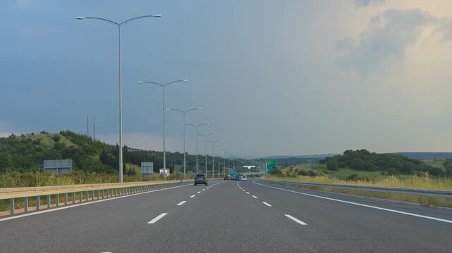 Car drives on a daytime highway passing a large green directional road sign under cloudy summer sky