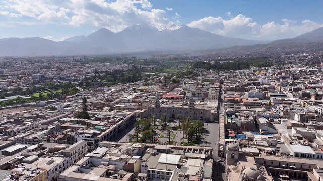 Aerial drone footage of Plaza de Armas in Arequipa, Peru, featuring the Basilica Cathedral and the iconic Misti volcano in the background under a bright blue sky.