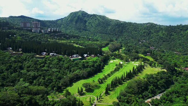 Cinematic forward drone flight over Woodridge Place in Tagaytay Highlands revealing landscaped gardens, luxury accommodations, golf course, mountain and surrounding natural scenery during daylight.