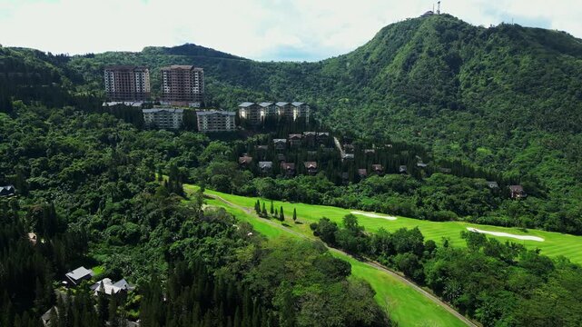 Wide establishing aerial shot of Woodridge Place at Tagaytay Highlands in Cavite Philippines showcasing luxury lodging surrounded by lush forests, landscaped golf course and high rises building.