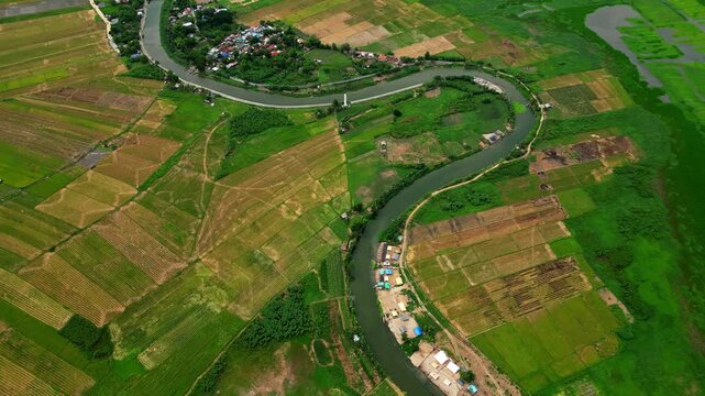 Wide angle aerial shot featuring green rice fields divided by the winding Morong River with its distinctive S-shaped formation in Sitio Wawa Community, Morong, Rizal, Philippines during daylight.