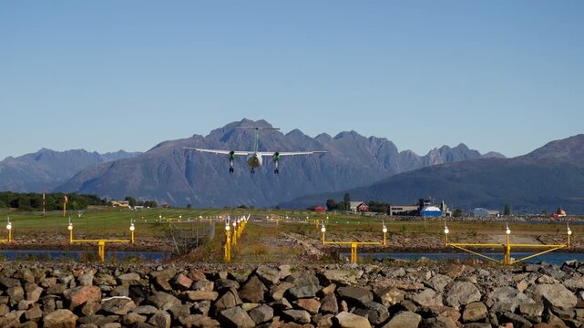 Scheduled regional passenger aircraft on final approach to land at Stokmarknes Airport, Norway. Scenic aviation footage featuring mountain landscapes, transport infrastructure, and air travel