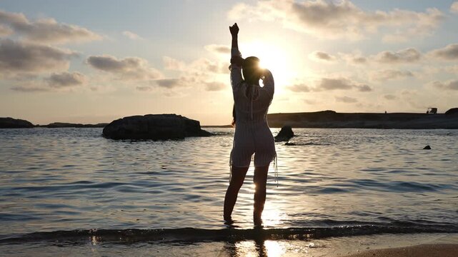 Silhouette of a graceful woman dancing on a beach at sunset