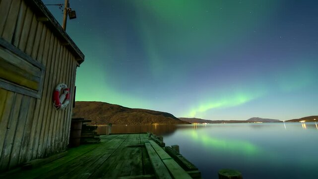 Aurora borealis swirling in night sky viewed from Nordic wooden dock. Timelapse