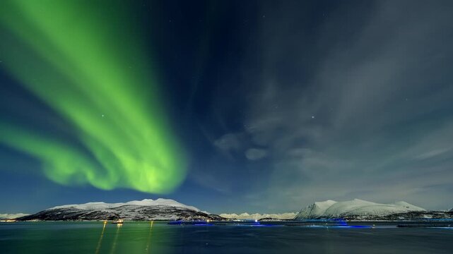 Nightlapse. Swirling green northern lights over snowy mountains and salmon farm