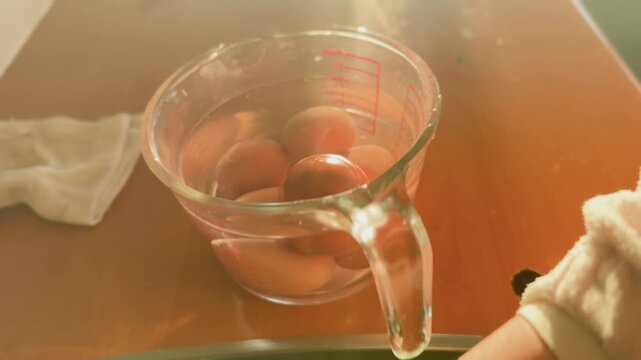 Freshly boiled eggs resting in hot water inside a glass measuring jug, illuminated by warm morning sunlight in a home kitchen.