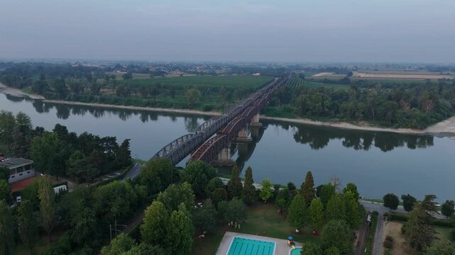 Ponte di Ferro crossing the Po River between Cremona, Lombardy, and Castelvetro Piacentino, Emilia-Romagna, Italy, with Canottieri Leonida Bissolati outdoor swimming pool in the foreground, aerial
