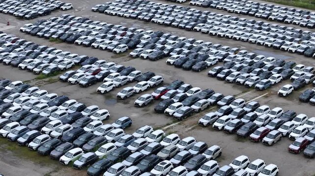 Thousands of parked passenger vehicles arranged in organized storage rows at a large automobile logistics yard, highlighting fleet distribution and automotive supply chain operations, drone forward
