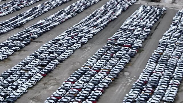 Finished crossover SUVs occupy dense storage rows at a large automotive logistics compound awaiting transport, dealer allocation and wholesale distribution, aerial pan.