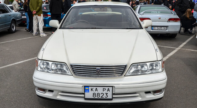 Pearl white Toyota Mark II sedan in clean, stock condition. This classic JDM executive car parked at an outdoor car festival in Kyiv