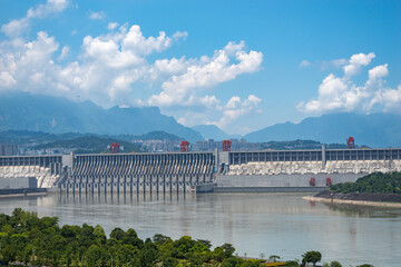 The massive concrete dam of the Three Gorges Reservoir Area in China stands across the river under a blue sky with white clouds on a sunny day © AS_SleepingPanda