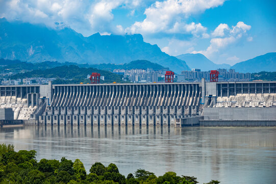 A view of the large concrete dam structure located within the Three Gorges Reservoir Area in China showing the calm water and mountain landscape under a blue sky