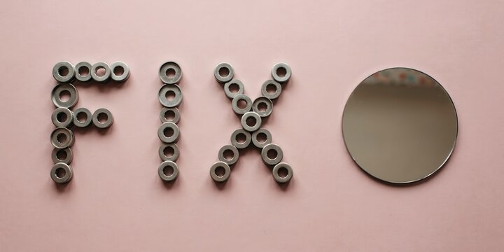 Objects spelling FIX with small metal washers next to a metal disc on pink background