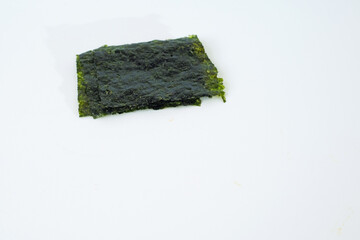 Several sheets of dark green seaweed rests on white background. Texture appears slightly rough and naturally frayed at edges. Minimalist composition emphasizes products natural appearance © Nurma
