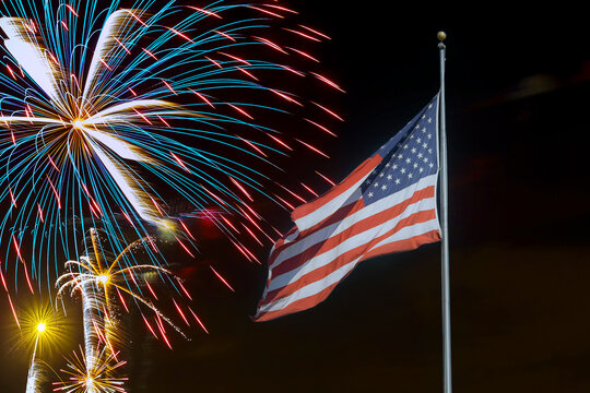 Fireworks display behind American flag during celebration at night in July