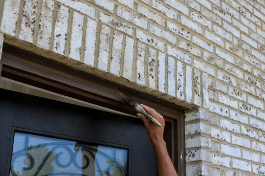 Person paints wooden trim on brick wall around door in residential area
