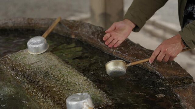 Hands pouring water from ladle at stone purification basin at Japanese temple