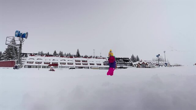 A child in colorful winter clothes walks and flings snow across a snowy resort landscape under an overcast sky in Las Le&ntilde;as, Mendoza, Argentina.