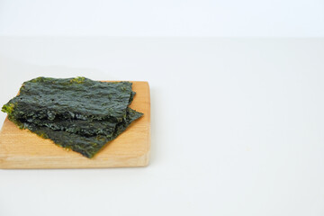Fresh seaweed sheets rest on a light wooden board. Simple, clean background highlights natural texture and color. Ideal for health, wellness, or Asian cuisine content © Nurma
