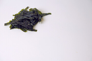 Dark green seaweed pieces lie scattered. They rest on a plain white background. The texture appears dry and brittle. Natural, organic shape with irregular edges. Suitable for food, health © Nurma