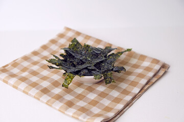 Fresh seaweed rests on a checkered cloth. Simple, clean background enhances the natural texture. Minimalist composition draws focus to the organic form. Ideal for health, wellness, or culinary themes © Nurma