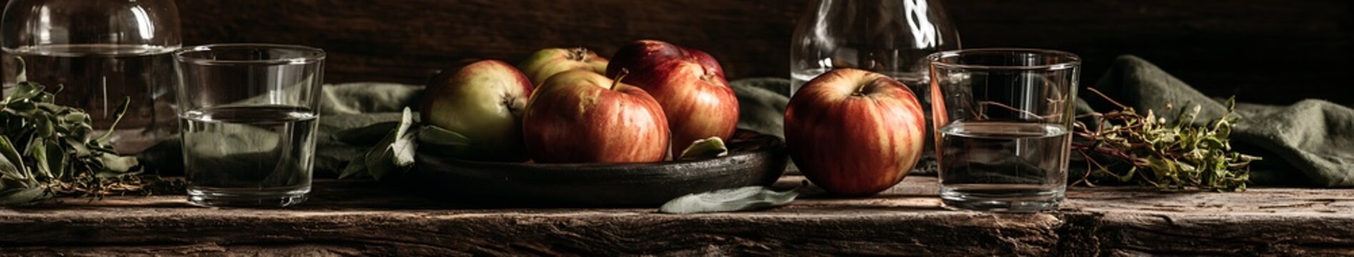 Fall Food And Drink Rustic still life of red and green apples in wooden bowl with glassware, herbs on weathered table