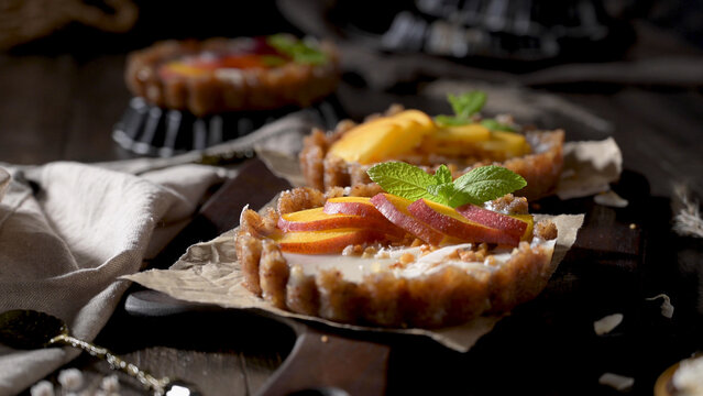 Mini peach tarts with creamy filling and mint on a rustic wooden board