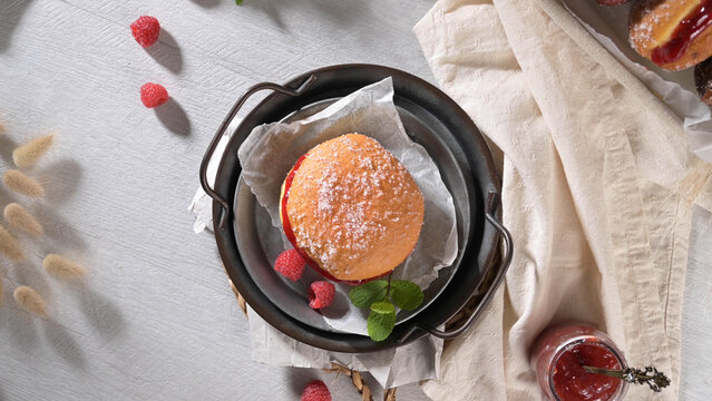 Top down view of a sugar dusted jam filled donut with fresh raspberries in a rustic metal tray