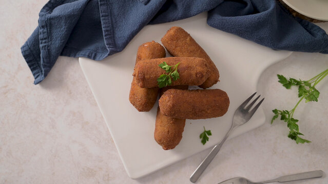 Golden fried breaded croquettes on a white plate with fresh parsley
