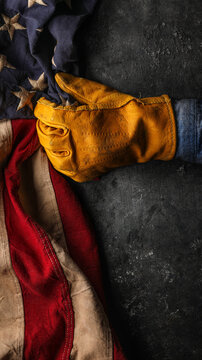 Worn yellow work glove pulling the American flag. Symbolic of blue collar workers, USA manufacturing, pride in products Made in United States of America, or to celebrate Father's day or US Labor Day.