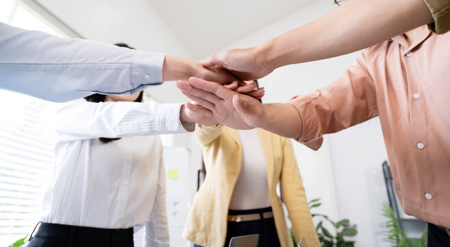Close-up of business people stacking hands together in office for teamwork and unity.