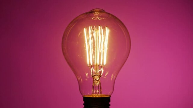 Bright retro style lightbulb illuminated against vibrant magenta background in artistic close up.