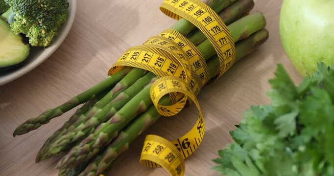 Measuring tape and healthy products on wooden table, closeup. Camera moving right