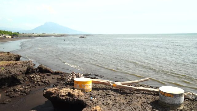 muddy beach shore with buckets and wooden pole by water
