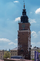 Wieża ratuszowa na historycznym Rynku Starego Miasta w Krakowie w słoneczny wiosenny dzień. Zbudowana z cegły, wieża ma zegar i czarną kopułę dzwonnicy zwieńczoną iglicą, odcinającą się od nieba . © Grzegorz