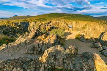 Golden afternoon light on rocky canyon rim with interpretive sign and shrubs above the Gunnison gorge, Black Canyon of the Gunnison NP, Colorado. © ZL Visuals