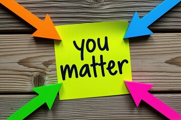 Yellow sticky note with handwritten matter text on wooden surface. Bright colorful arrows point at paper message. Motivation concept for mental health, support. Positive psychology reminder for self
