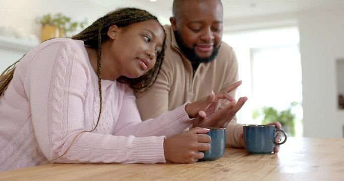 African couple at kitchen counter, woman showing left hand while man examining hand with blue mugs