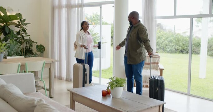 African couple arriving through sliding glass door into living room, carrying suitcases and smiling