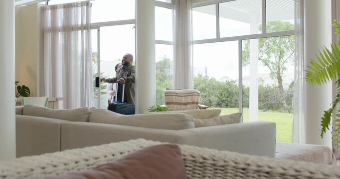 African American couple entering through sliding door, pulling wheeled suitcase, arriving home