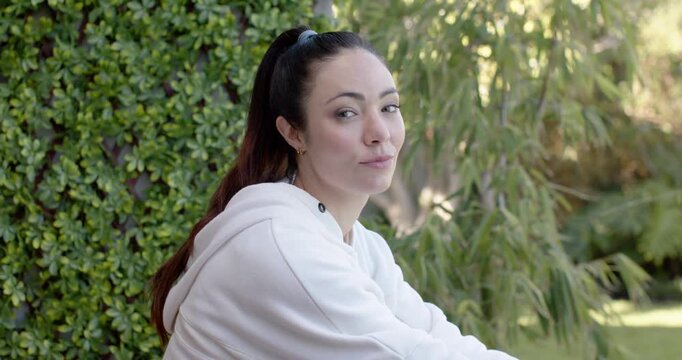 Adult woman pausing to breathe, opening eyes, turning head, smiling at camera in garden hedge