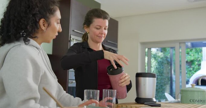 Diverse women seeing right woman taking pink blender cup twisting lid pouring into glasses to share