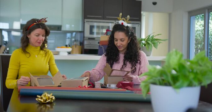 Diverse female friends in yellow and pink sweaters opening boxes, sorting ribbons, preparing gifts