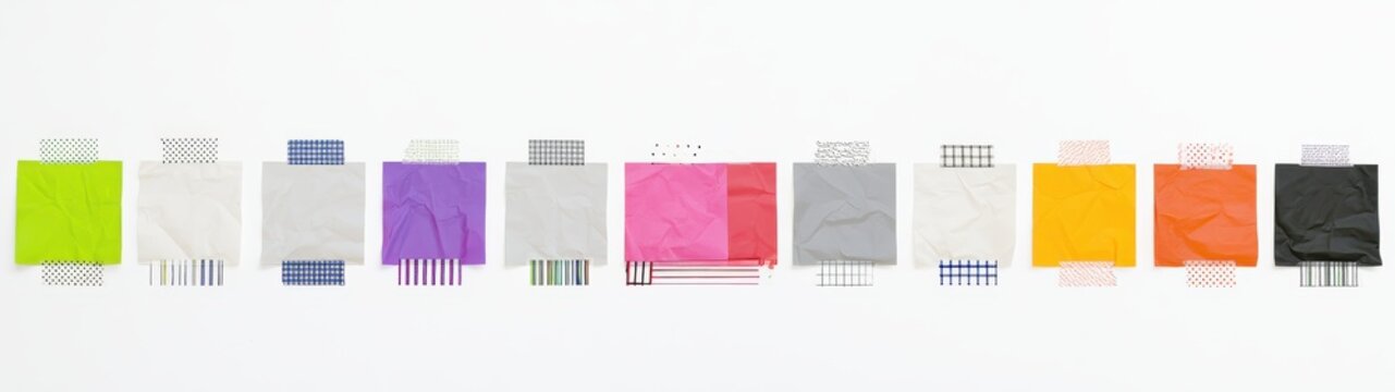 An ultra-wide panoramic studio photograph featuring a chronological line of ten identical, slightly crumpled paper squares arranged horizontally, each attached with different patterned washi tapes
