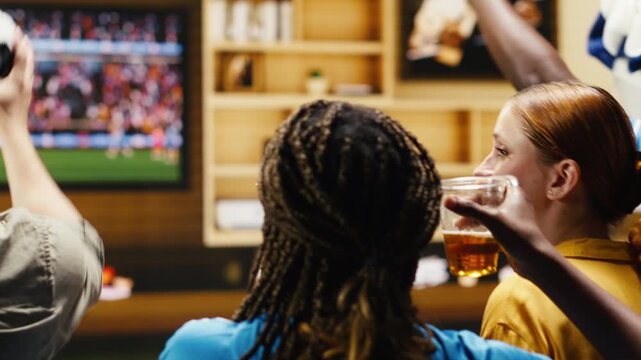 Tight framing shows soccer fans holding popcorn bowl, ball and team scarves during home watch party on sofa while football supporters use match day props while following live game TV broadcast.