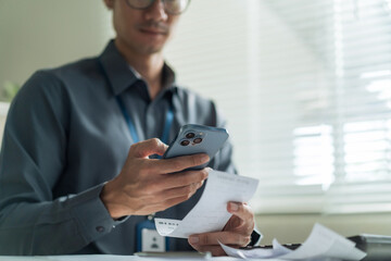 Close-up of office worker using smartphone to scan receipt and financial bill for mobile payment at desk. © wanakit