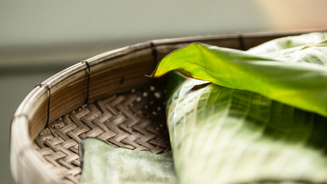 Close-up of fresh green banana leaves on a traditional woven bamboo basket.
