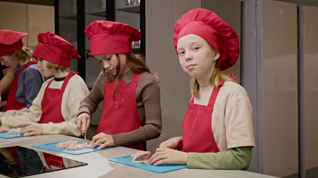 Medium portrait of Caucasian teenage girl wearing chef hat and apron, slicing raw meat during culinary class. Clip is perfect for marketing youth cooking workshops or educational programs