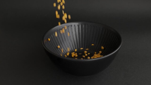 Pouring yellow lentils into black bowl dark background 4k