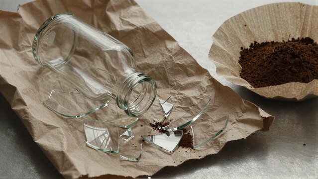 Broken glass jar spills coffee grounds on brown paper, symbolizing loss or destruction.